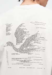 Biała bawełniana koszulka z nadrukiem tekstowym na plecach, przedstawiającym różne frazy i nazwy ułożone w graficzny wzór.