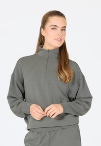 Ljust grå tröja med hög krage och halvdragkedja. Har en avslappnad passform och mjukt material, kombinerad med matchande sweatpants.