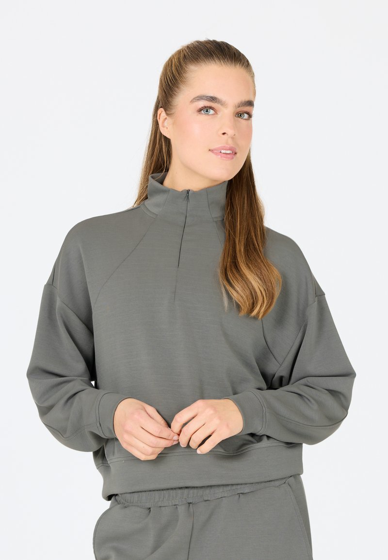 Ljust grå tröja med hög krage och halvdragkedja. Har en avslappnad passform och mjukt material, kombinerad med matchande sweatpants.
