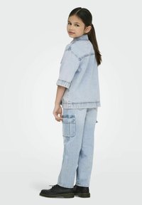 Ljusblå denimoutfit med en kortärmad skjorta och cargobyxor med fickor. Svarta snörkängor fulländar looken.