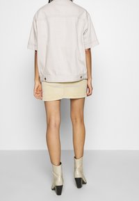 Giacca di jeans oversize colore beige chiaro con maniche corte, abbinata a una mini gonna in velluto a coste beige e stivaletti argento texturizzati.