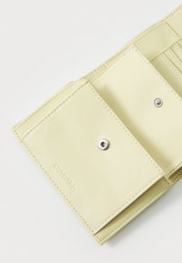 Le portefeuille jaune Calvin Klein est fabriqué en matière synthétique lisse, dispose d'une fermeture à pression, de plusieurs emplacements pour cartes et arbore le nom de la marque en relief sur le devant.