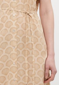 Beige dress with a shell pattern, featuring a tie belt, buttons down the front, and a smooth, lightweight fabric texture.