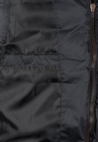 Schwarze Steppjacke mit glatter, glänzender Textur, Reißverschluss vorne mit bronzefarbenen Beschlägen und einer externen Tasche auf der linken Seite.