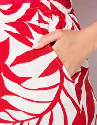 Rood en witte stof met grote bladdessins, met een elastische tailleband en een hand in een zijzak.