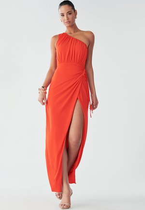 Model poses in a one-shoulder orange dress with a thigh-high slit, showcasing a sleek silhouette and elegant style, paired with neutral heels.