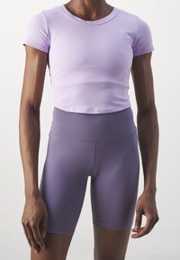 Person wearing a fitted lilac short-sleeve crop top and high-waisted purple biker shorts against a plain background.