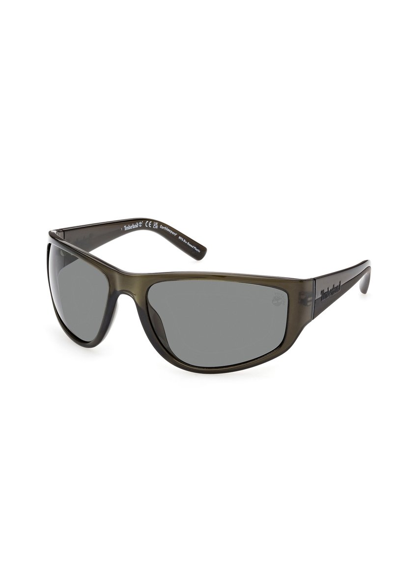 Gafas de sol con montura de plástico gris verdoso, lentes gris oscuro y diseño aerodinámico envolvente. Presenta el logotipo de Timberland en las patillas.