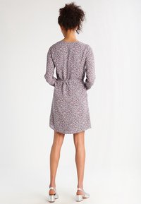 Robe à imprimé floral avec des manches longues, taille cintrée et ourlet arrondi. Présente un motif de petites fleurs rouges et bleues sur un fond clair.