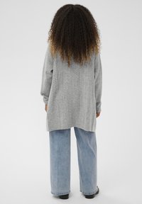 Szürke, texturált bordázott mintájú kötött pulóver világoskék, bő szárú farmerrel és fekete cipővel párosítva. Hátsó nézeten hosszú ujjakkal és ívelt szegéllyel.