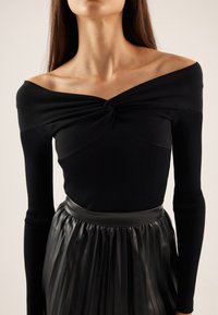 Haut noir à manches longues côtelé avec un design épaules dénudées et un détail twist à l'avant, associé à une jupe en cuir noire plissée avec une taille lisse.