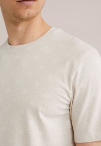 Beige, rövid ujjú póló, diszkrét gyémántmintázattal, kerek nyakkivágással és puha, sima szövettextúrával.
