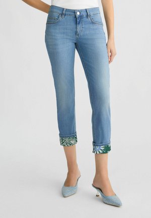 Jean en denim bleu clair avec une coupe courte, présentant des poignets en tissu vert et à motifs, cinq poches et une fermeture à bouton.