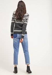 Neulottu musta ja harmaa neulepaita, jossa on kuvioitu hartialeikkaus ja pitkät hihat, yhdistetty vaaleansinisillä käännetyillä reunahousuilla ja mustilla nilkkureilla.