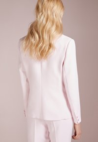 Vaaleanpunainen räätälöity bleiseri, jossa on sileä pinta, pitkät hihat ja hillityt napin yksityiskohdat hihoissa. Siisti ja nykyaikainen leikkaus.