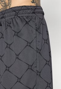 Grå treningsshorts med et subtilt svart geometrisk mønster, med elastisk midjebånd og side-lomme for enkelhet.