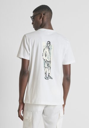 Uomo con maglietta bianca e pantaloncini cargo visto di spalle; sul retro della maglietta è presente una figura schizzata di una persona con abiti casual e cappellino.