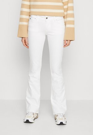 Person trägt weiße Schlagjeans, beige-weiß gestreiften Pullover mit breiten Bündchen und weiße Turnschuhe mit beigen Akzenten.