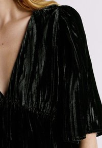 Robe en velours noir avec un décolleté en V profond, des manches courtes à volants et un tissu texturé avec des rayures verticales. Détail de taille élastique inclus.