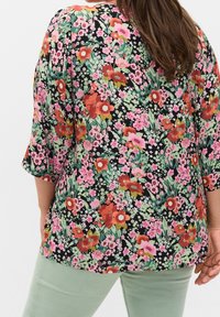Blusa floral en negro con flores vibrantes en rojo, rosa y verde; corte relajado, mangas tres cuartos, tela ligera, diseño casual.