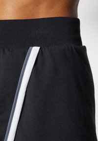 Svarta träningsshorts med en ribbad midja och en vit och grå sidostrandetail. Tyget verkar mjukt och smidigt.