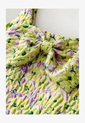 Floral dress with a yellow-green base, featuring a bow detail. The fabric has a soft texture with raised floral patterns in pink and green.