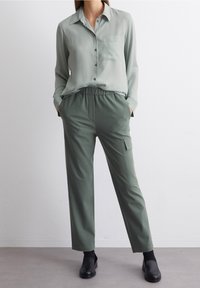 Lys grøn, kravebutton-up skjorte med lomme, parret med olivengrønne, elastiske cargo-bukser med sidelommer. Sorte sko.
