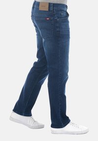 Jeans de mezclilla azul con corte recto, con bolsillos traseros y una etiqueta de cuero marrón en la cintura. Llevados con zapatillas blancas.