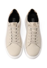 Sneakers in pelle beige con una texture liscia, punta arrotondata, suola piatta bianca e lacci abbinati. Accenti dorati sulla linguetta e sul logo.