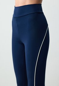Leggings blu navy con vita alta, texture liscia e una striscia laterale bianca a contrasto per un tocco in più. Progettati per comfort e movimento.
