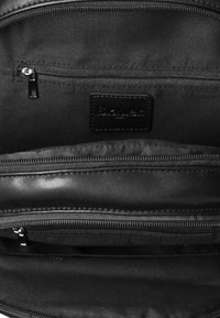 Interno di borsa in pelle nera con molte tasche con cerniera, texture liscia e etichetta in pelle con marchio. Il tessuto interno è scuro e opaco.