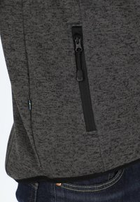 Donkergrijze sweatshirt met een gestructureerde stof, voorzien van een zwarte ritszak en een klein gekleurd label aan de zoom.