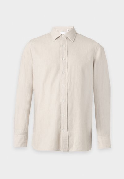Chemise beige à manches longues, boutonnée devant, avec un col pointu, sur un fond uni.
