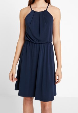Robe bleu marine sans manches, longueur genou, avec fines bretelles, taille froncée et détail plissé à l'encolure, portée par une personne debout.