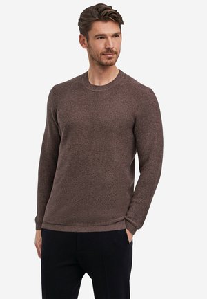 Bruine gebreide trui met een ronde hals, ribgebreide manchetten en zoom. Heeft een gestructureerde afwerking en een slim fit ontwerp. Gedragen over donkere broeken.