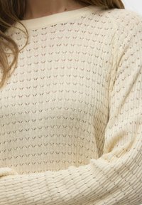 Maglione a maglia crema chiara con un motivo testurizzato di piccoli fori, polsi a coste e scollo rotondo. Tessuto morbido con una vestibilità comoda.