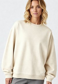 Felpa oversized beige con scollo rotondo e polsi a costine, realizzata in tessuto morbido con una finitura leggermente testurizzata.