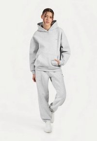 Sudadera con capucha gris y pantalones deportivos a juego hechos de material de forro polar; cuentan con un bolsillo delantero, capucha con cordón y puños acanalados para mayor comodidad.