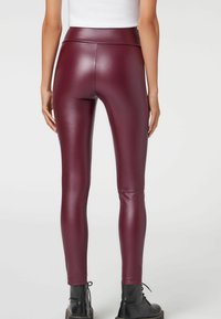 Leggings en simili cuir bourgogne avec une taille haute, un design ajusté et une texture lisse, associés à des bottes noires à lacets.