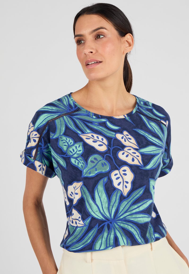 T-shirt azzurro a maniche corte con grandi motivi di foglie tropicali verdi e scollatura rotonda. Tessuto morbido con risvolti sulle maniche e dettagli di cucitura discreti.