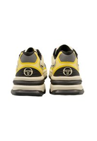 Scarpe sportive nere e gialle con upper testurizzato, colletto imbottito e suola grigia spessa; presenta un dettaglio del logo sul tallone.