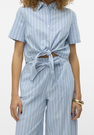 Lichtblauw shirt met korte mouwen en witte verticale strepen, vooraan geknoopt, gecombineerd met bijpassende hooggesneden wijde broekspijpen.