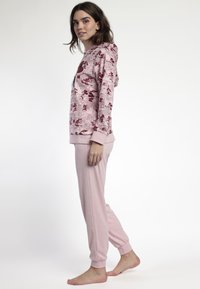 Sudadera rosa con estampados de cómic, combinada con joggers de un rosa claro. Ambos tienen una tela suave y texturizada y puños acanalados en los tobillos y las muñecas.