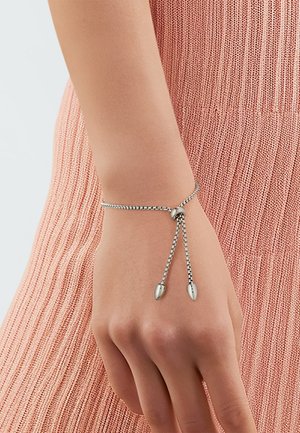 Silver chain bracelet with adjustable length, featuring two pointed accents at the ends. The background is a textured pink fabric.