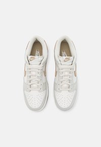 Bílé kožené tenisky se světle béžovými akcenty, perforovanou špičkou a béžovými tkaničkami. Na boku je jemný přechodový vzor.