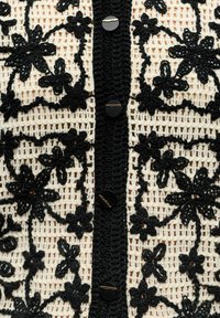 Gros plan d'un tissu crocheté noir et blanc avec des motifs floraux et quatre boutons noirs alignés verticalement au centre.
