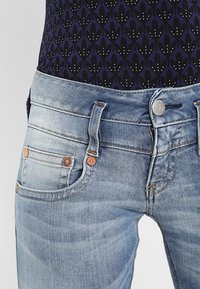 Jeans in denim azzurro chiaro con vita media, design a cinque tasche, rivetti in rame a contrasto e texture sbiadita nella parte anteriore.