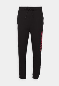 Pantalones deportivos negros con cinturilla elástica y cordón. Presenta el logo rojo "HUGO" en la pierna izquierda. Hechos de una tela suave y lisa.