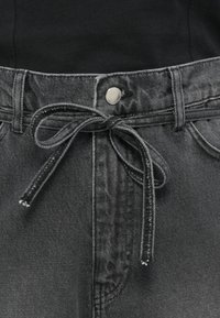 Svarte denimbukser med knyttet midje, metallknapp og subtil tekstur, med en klassisk fem-lommers design.