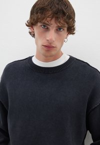 Maglione lavorato a maglia di un blu navy scuro con un collo a girocollo a coste e una trama sottile. Indossato sopra una camicia bianca a manica lunga, con una vestibilità rilassata.